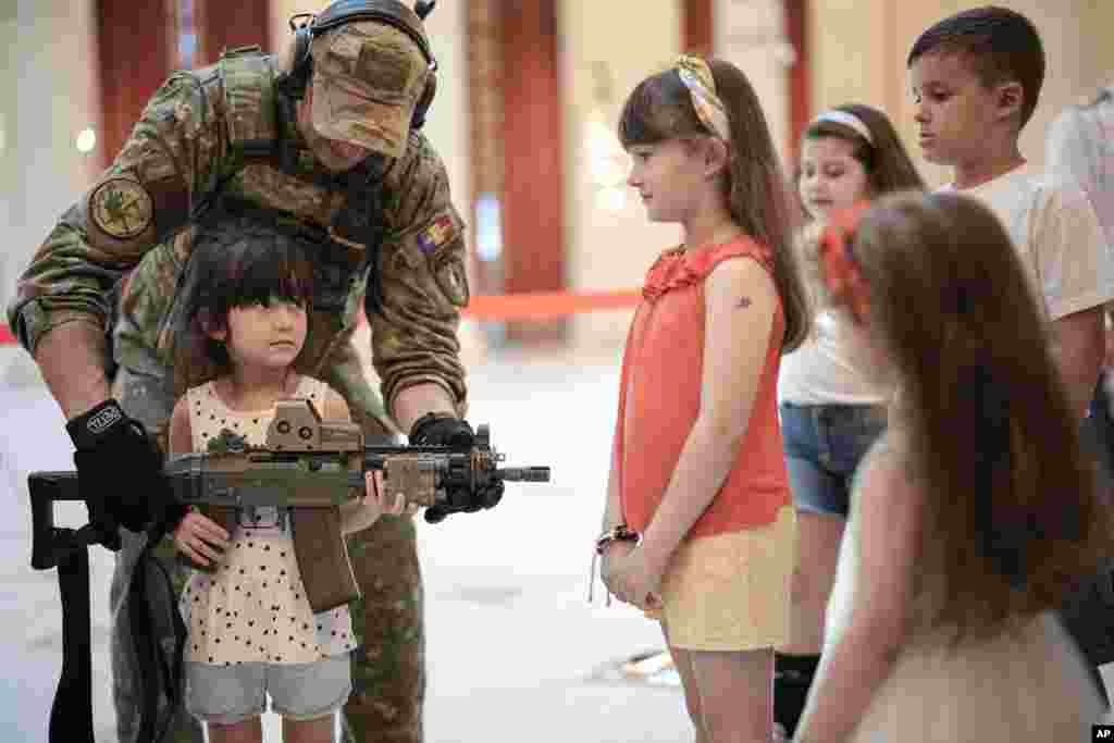 A girl poses with a weapon at a stand set up by Romania&#39;s army special forces at the Palace of the Parliament on International Children&#39;s Day in Bucharest.