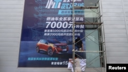 FILE - Workers put on a giant poster for government subsidies for Dongfeng Peugeot cars at a dealership in Wuhan, Hubei province, China, Aug. 9, 2020. 