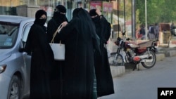 Women wearing hijabs stand along a street in Kabul on May 7, 2022.