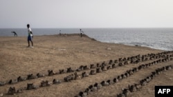 Des hommes s'étirent devant une installation artistique de l'artiste sénégalais Yakhya Ba, le long de la promenade maritime de Dakar, le 11 mai 2022.