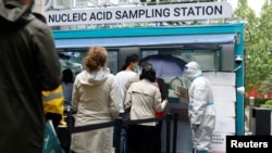 5月6日，北京市民冒雨在一流动新冠病毒核酸检测站前排队等候检测，一名身穿防护服的工作人员在维持秩序。-路透社照