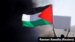Seorang Palestina mengibarkan bendera Palestina saat protes anti-Israel atas kekerasan lintas perbatasan antara militan Palestina di Gaza dan militer Israel, 18 Mei 2021.