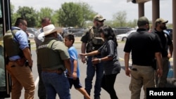 A child gets on a school bus as law enforcement personnel guard the scene of a shooting at Robb Elementary School in Uvalde, Texas, May 24, 2022.