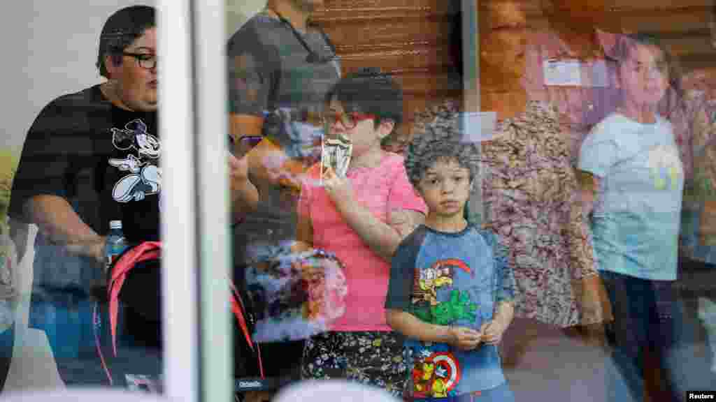 A child looks on through a glass window from inside the Ssgt. Willie de Leon Civic Center, where students had been transported from Robb Elementary School after a shooting, in Uvalde, Texas, May 24, 2022.