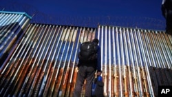 FILE - A migrant waits of the Mexican side of the border after United States Customs and Border Protection officers detained a couple of migrants crossing the US-Mexico border on the beach, in Tijuana, Mexico, Jan. 26, 2022.