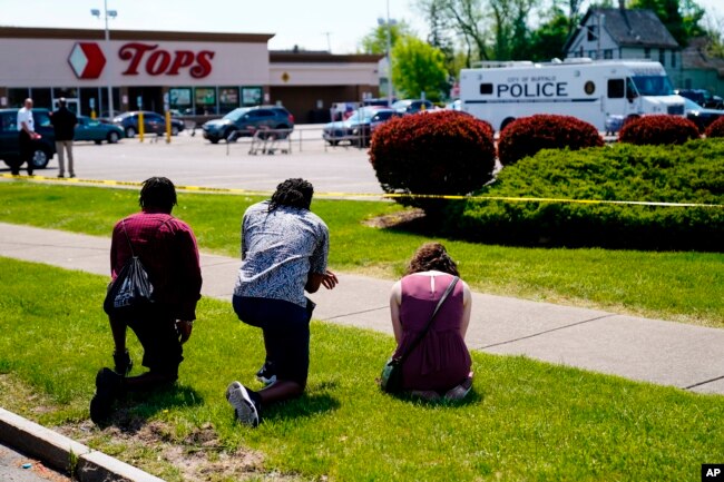 People pray outside the scene of Saturday's shooting at a supermarket, in Buffalo, N.Y., May 15, 2022. The shooting is the latest example of targeted racial violence. (AP Photo/Matt Rourke)