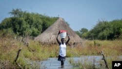 FILE - A woman carries a bucket on her head as she wades through floodwaters in the village of Wang Chot, Old Fangak county, Jonglei state, South Sudan on Nov. 26, 2020.