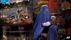 Una mujer con burka camina por un mercado de pájaros mientras carga a su hijo, en el centro de Kabul, Afganistán, el domingo 8 de mayo de 2022.