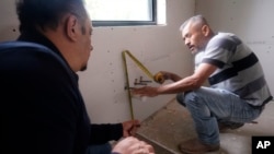 Tile subcontractor Horacio Gomez, right, originally from the Mexican state of Michoacan, measures and talks with homebuilder Joshua Correa about plans at a custom home under construction in Plano, Texas, Tuesday, May 3, 2022.