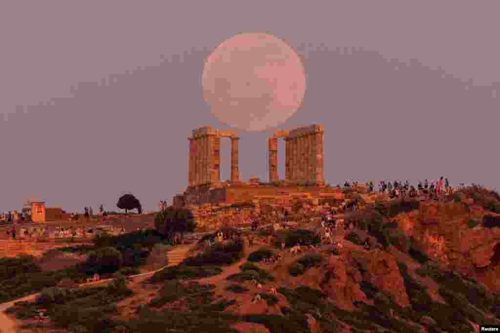 People watch a full moon, known as the &quot;Flower Moon,&quot; rising behind the Temple of Poseidon, before a lunar eclipse in Cape Sounion, near Athens, Greece, May 15, 2022.