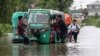 Orang-orang mendorong bemo di jalanan yang tergenang banjir dan seorang anak sekolah mengendarai sepedanya di daerah Bagha di Sylhet, Bangladesh, Senin, 23 Mei 2022. (AP)