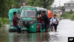 Orang-orang mendorong bemo di jalanan yang tergenang banjir dan seorang anak sekolah mengendarai sepedanya di daerah Bagha di Sylhet, Bangladesh, Senin, 23 Mei 2022. (AP)