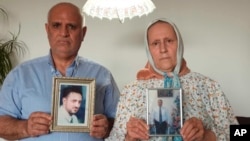 This photo provided by the Siyam family, shows Omar, left, and Siham Siyam, holding portraits of their son, Wassim Siyam, who was shot dead by Syrian soldier agents, at their home, in Germany, May 11, 2022.