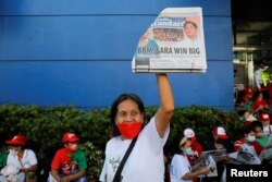 Seorang pendukung kandidat presiden Ferdinand "Bongbong" Marcos Jr. mengangkat sebuah surat kabar dengan judul utama kemenangan Marcos Jr., saat orang-orang berkumpul untuk merayakan sebagai hasil sementara Pilpes 2022. (Foto: Reuters)