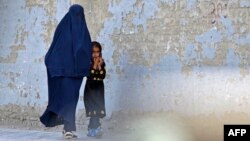 FILE - A burqa-clad woman walks with a girl along a street in Kabul on May 7, 2022. 