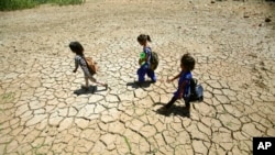 FILE - Children returning from school walk through a dried pond on a hot summer day on the outskirts of Jammu, India. May 30, 2019. With heat waves becoming more common, demand for safety-net programs is growing.