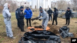 FILE - French forensics investigators, in Ukraine to investigate war crimes amid Russia's invasion, stand next to a mass grave in the town of Bucha, in Kyiv region, Ukraine, April 12, 2022. 
