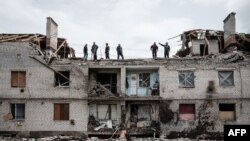 Workers clean rubbles atop a buidling destroyed by shelling a month ago in Cherkaske, eastern Ukraine on May 11, 2022. 