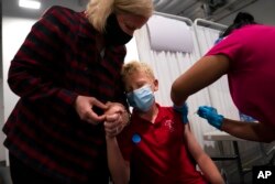 FILE - A mother holds the hand of her 12-year-old son as he receives the first dose of the Pfizer COVID-19 vaccine at the Providence, Edwards Lifesciences vaccination site in Santa Ana, Calif., May 13, 2021.
