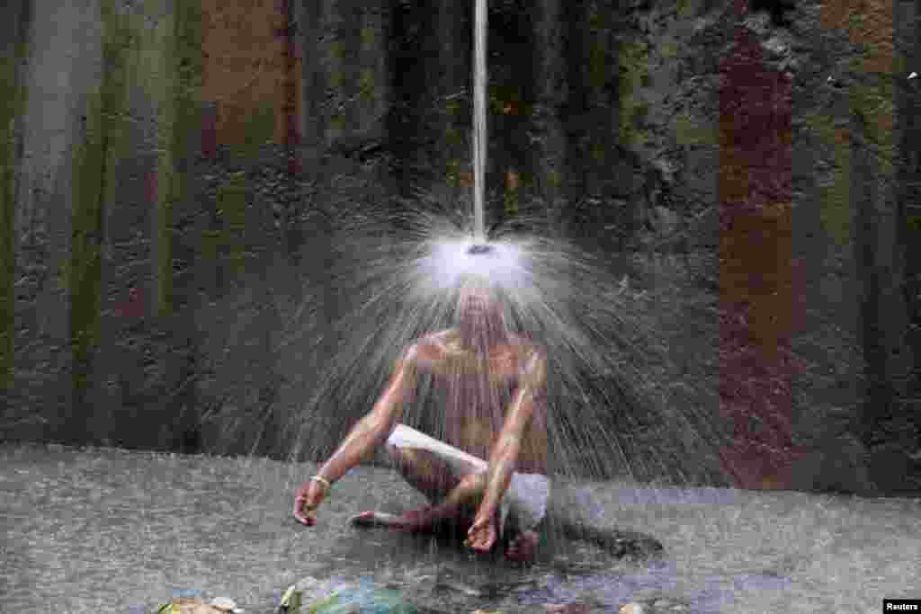 A man cools off under a pipe of flowing water on a hot summer day in New Delhi, India.