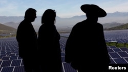 FILE - Locals walk past solar panels during the opening ceremony of the largest solar power plant of Chile's capital, in Santiago July 19, 2017. (REUTERS/Ivan Alvarado)