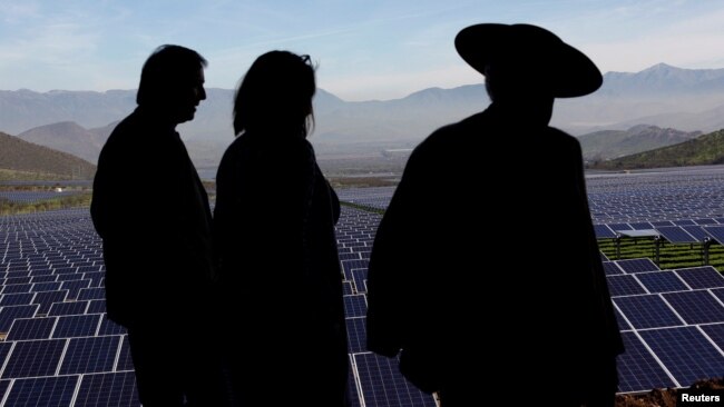 FILE - Locals walk past solar panels during the opening ceremony of the largest solar power plant of Chile's capital, in Santiago July 19, 2017. (REUTERS/Ivan Alvarado)