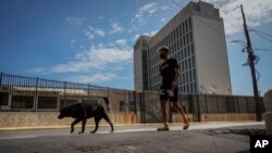 Un hombre y su perro pasan frente a la embajada de Estados Unidos el día después de que reabrió sus servicios consulares en La Habana, Cuba, el miércoles 4 de mayo de 2022.