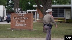 Un officier marche devant la Robb Elementary School à Uvalde, après la fusillade d'un jeune homme ayant tué des enfants et des enseignants dans une école primaire du Texas le 24 mai 2022. (Photo AFP Allison Dinner)