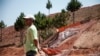 FILE - A man stands by a mining machine that filters the dirt containing gold inside the Chinese company Jiuxing's mine at Soamahamanina, Madagascar, on Oct. 7, 2016.