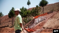 FILE - A man stands by a mining machine that filters the dirt containing gold inside the Chinese company Jiuxing's mine at Soamahamanina, Madagascar, on Oct. 7, 2016.