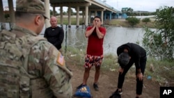 Three migrants from Cuba stand in front of a National Guardsman after crossing the Rio Grande river in Eagle Pass, Texas, May 22, 2022.