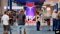 People gather at booths near some of the signage in the hallways outside of the exhibit halls at the NRA Annual Meeting held at the George R. Brown Convention Center , May 26, 2022, in Houston.