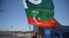 Seorang pendukung partai Pakistan Tehreek-e-Insaf (PTI), mengibarkan bendera di samping kontainer yang ditumpuk oleh pihak berwenang untuk memblokir Zona Merah menjelang aksi duduk yang direncanakan di Islamabad pada 24 Mei 2022. ( Aamir QURESHI / AFP)