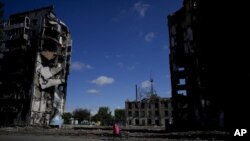 Una mujer monta en bicicleta cerca de edificios destruidos por ataques en Borodyanka, a las afueras de Kiev, Ucrania, el martes 31 de mayo de 2022. (AP Foto/Natacha Pisarenko)