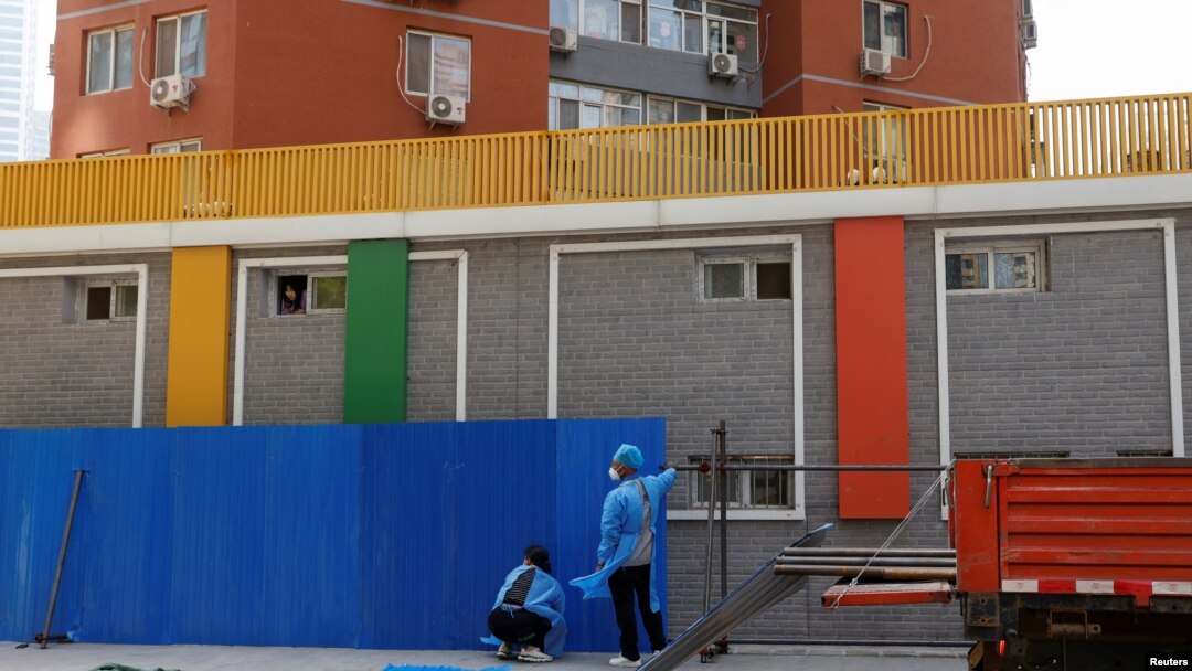 Workers wearing personal protective equipment (PPE), install a barricade around a residential area under lockdown while a resident looks out from a window, amid the coronavirus disease (COVID-19) outbreak in Beijing, China, May 4, 2022.