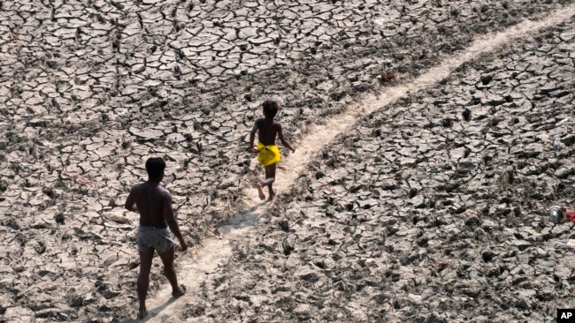FILE - A man and a boy walk across the drying bed of river Yamuna in India, May 2, 2022. According to a report released by the World Meteorological Organization on May 9, 2022, the world is creeping closer to the warming threshold international agreements are trying to prevent.