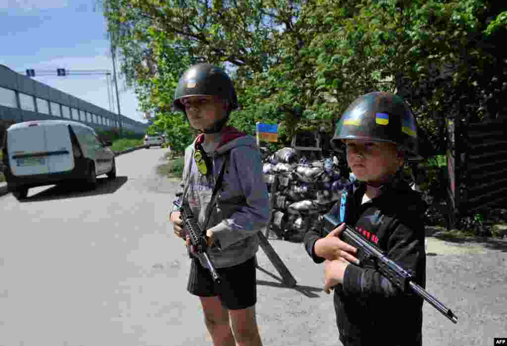 Anak-anak Ukraina bermain sebagai tentara pertahanan teritorial di &quot;pos pemeriksaan&quot; tiruan di desa Stoyanka, wilayah Kyiv, di tengah invasi Rusia ke Ukraina (19/5). (Foto: AFP)