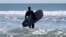 Dan Fischer, of Newport, Rhode Island, walks into the Atlantic Ocean with his surfboard in Newport on May 18, 2022. Fischer, 42, created the One Last Wave Project in January 2022 to use the healing power of the ocean to help families coping with a loss.
