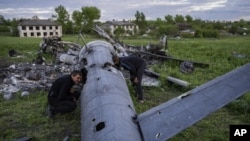 Oleksiy Polyakov, a la derecha, y Roman Voitko revisan los restos de un helicóptero ruso destruido en un campo en el pueblo de Malaya Rohan, región de Kharkiv, Ucrania, el lunes 16 de mayo de 2022. (Foto AP/Bernat Armangue)