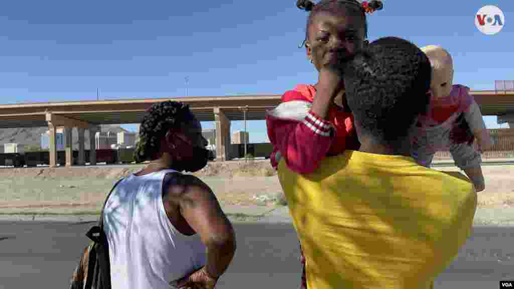 Familia haitiana evalúa la posibilidad de cruzar a El Paso, Texas, desde Ciudad Juárez. La pequeña de cinco años, sostiene a una muñeca en sus brazos mientras su papá la carga. Durante su espera ven cómo varias personas logran llegar al otro lado, pero finalmente desisten debido a la presencia de la Guardia Nacional.