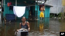 Edileuza Pereira da Silva lleva un plato con pescado para cocinar fuera de su casa, inundada por la crecida del río Negro el lunes 23 de mayo de 2022 en Iranduba, estado de Amazonas, Brasil. (AP Foto/Edmar Barros)