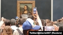 Visitors take pictures and video of the painting "Mona Lisa" after cake was smeared on the protective glass at the Lourve Museum in Paris, France, May 29, 2022 in this screen grab obtained from a social media video.
