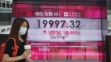 Una mujer con una mascarilla pasa frente al tablero electrónico de un banco que muestra el índice de acciones de Hong Kong en Hong Kong, el jueves 26 de mayo de 2022.