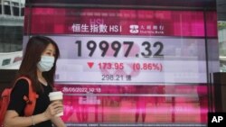 Una mujer con una mascarilla pasa frente al tablero electrónico de un banco que muestra el índice de acciones de Hong Kong en Hong Kong, el jueves 26 de mayo de 2022.
