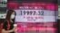 Una mujer con una mascarilla pasa frente al tablero electrónico de un banco que muestra el índice de acciones de Hong Kong en Hong Kong, el jueves 26 de mayo de 2022.