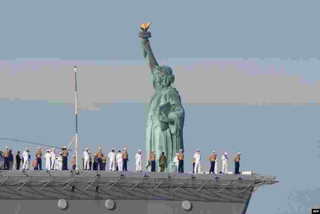 U.S. Sailors and Marines stand on the flight deck of the USS Bataan as the ship passes the Statue of Liberty during Fleet Week in New York Harbor.