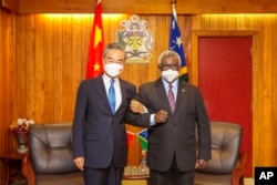 In this photo released by Xinhua News Agency, Solomon Islands Prime Minister Manasseh Sogavare locks arms with visiting Chinese Foreign Minister Wang Yi in Honiara, Solomon Islands, May 26, 2022.