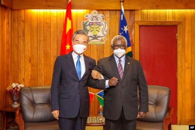 In this photo released by Xinhua News Agency, Solomon Islands Prime Minister Manasseh Sogavare locks arms with visiting Chinese Foreign Minister Wang Yi in Honiara, Solomon Islands, May 26, 2022.