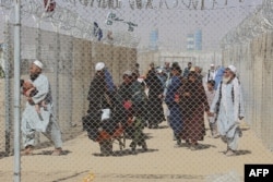 FILE - Afghan people walk inside a fenced corridor as they enter Pakistan at the Pakistan-Afghanistan border crossing point in Chaman, Aug. 25, 2021.