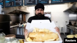 Owner of Hooked Fish and Chips shop, Bally Singh, holds a portion of fish and chips at his take-away in West Drayton, Britain, May 25, 2022. Picture taken May 25, 2022. (REUTERS/Peter Nicholls)